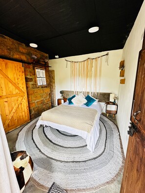 A cozy bedroom with a large bed, a wooden door, a stone wall, and a hanging tapestry.