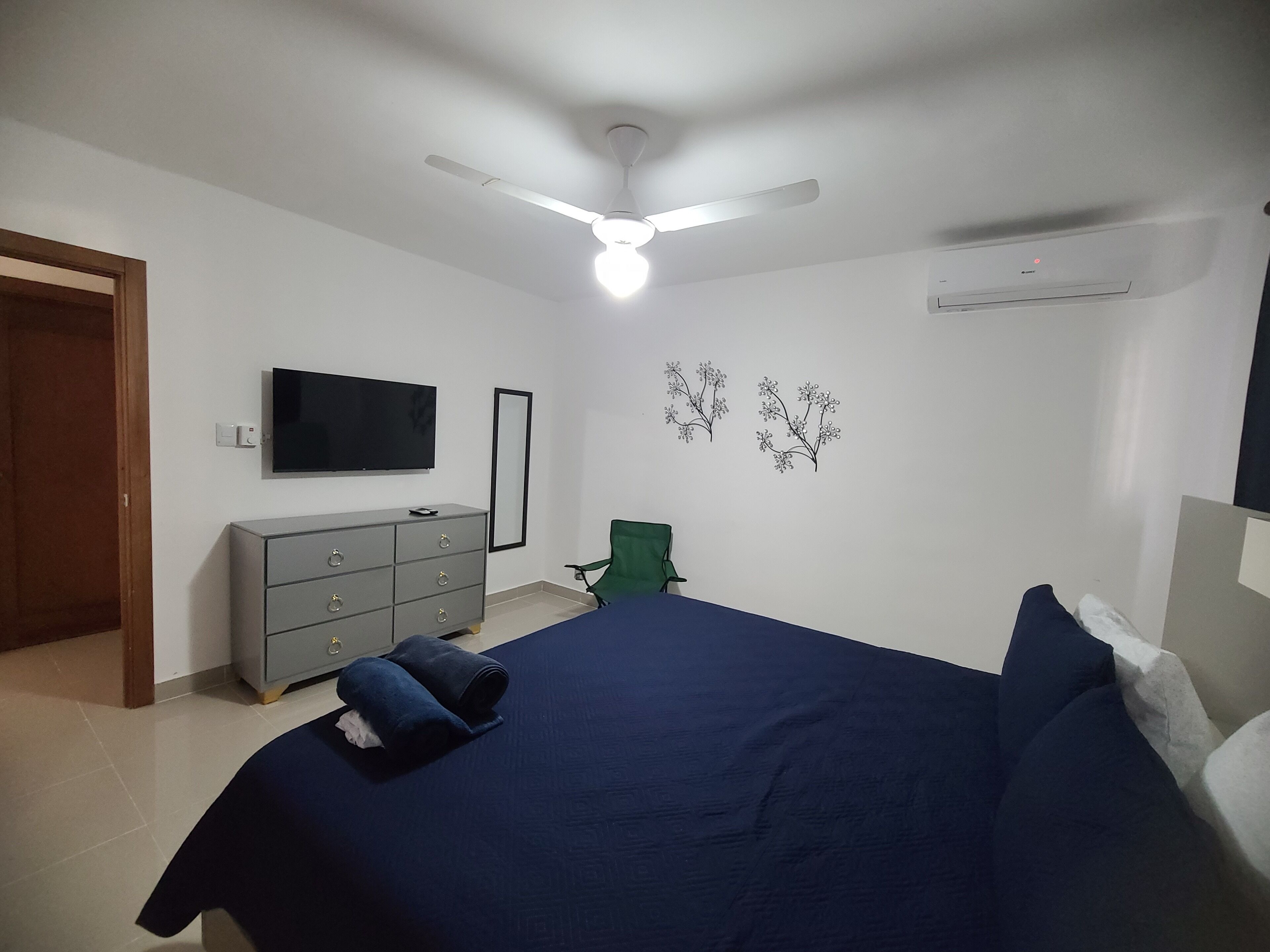 A bedroom with a bed, a dresser, a TV, a ceiling fan, and wall decorations.