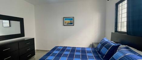 A bedroom with a bed, a ceiling fan, a window with curtains, a dresser, and a framed picture on the wall.