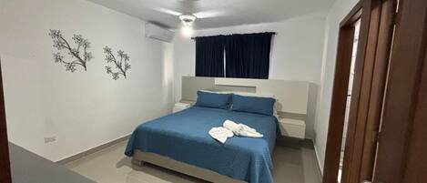 A bedroom with a bed, a bedside table, a nightstand, a ceiling fan, and a window with curtains.