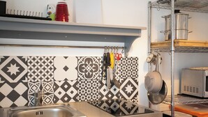 Een keuken met een roestvrijstalen spoelbak, een decoratieve achterwand en diverse keukengerei aan de muur.
