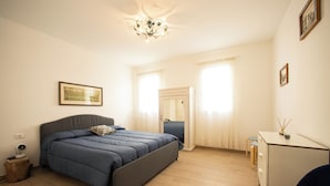 A bedroom with a bed, a desk, a chair, a mirror, and a chandelier.