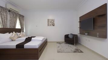 A bedroom with a bed, a TV mounted on the wall, a chair, and a small table.