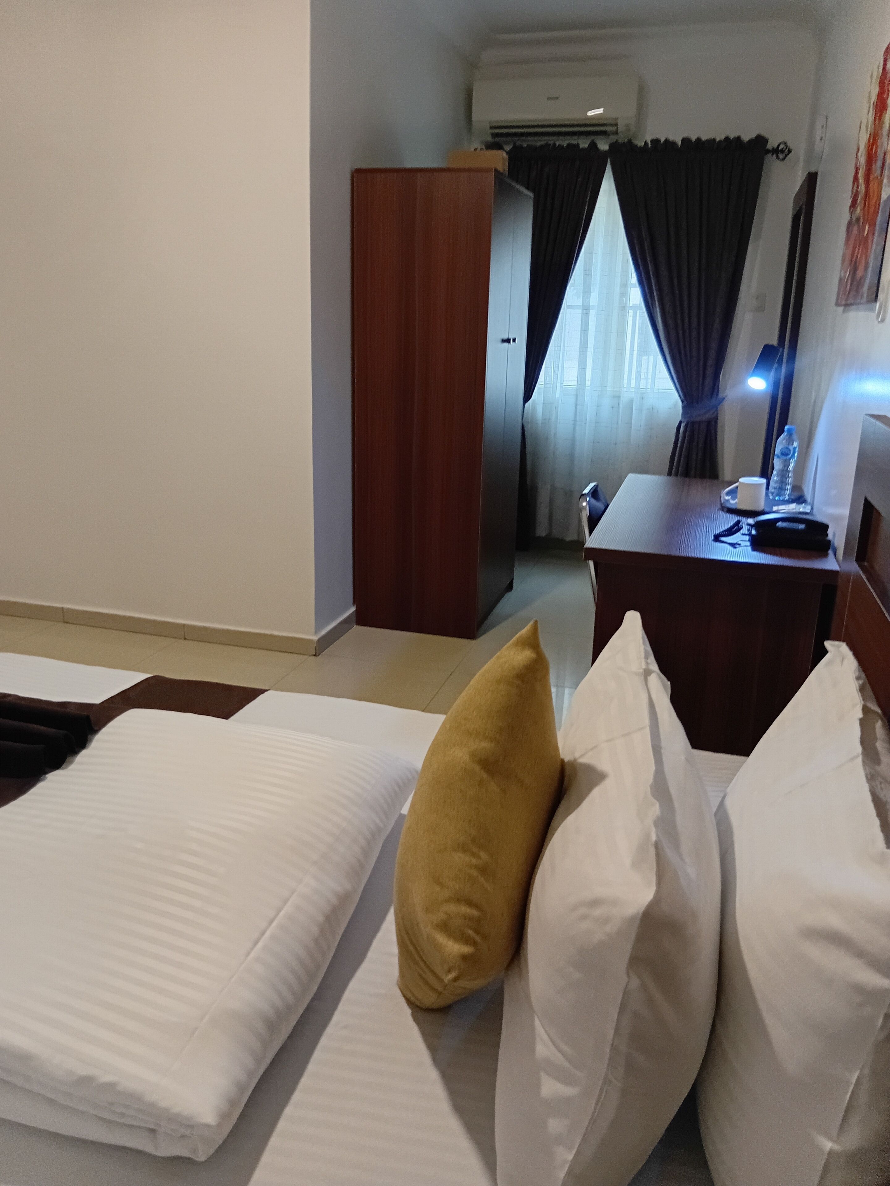 A hotel room with a bed, a desk, a wardrobe, and a window with curtains.