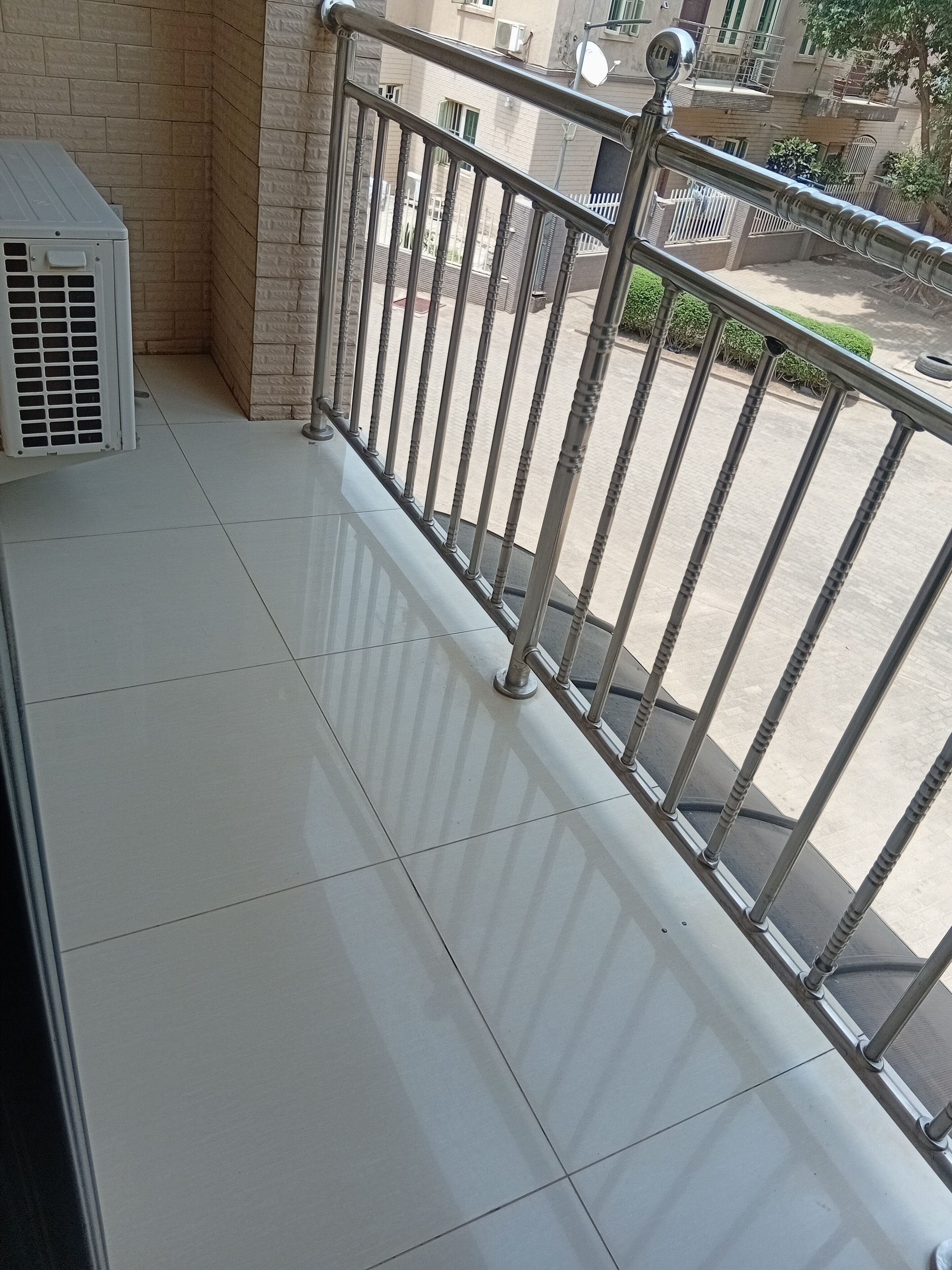 A balcony with a metal railing, a white air conditioning unit, and a view of a building with balconies and windows.