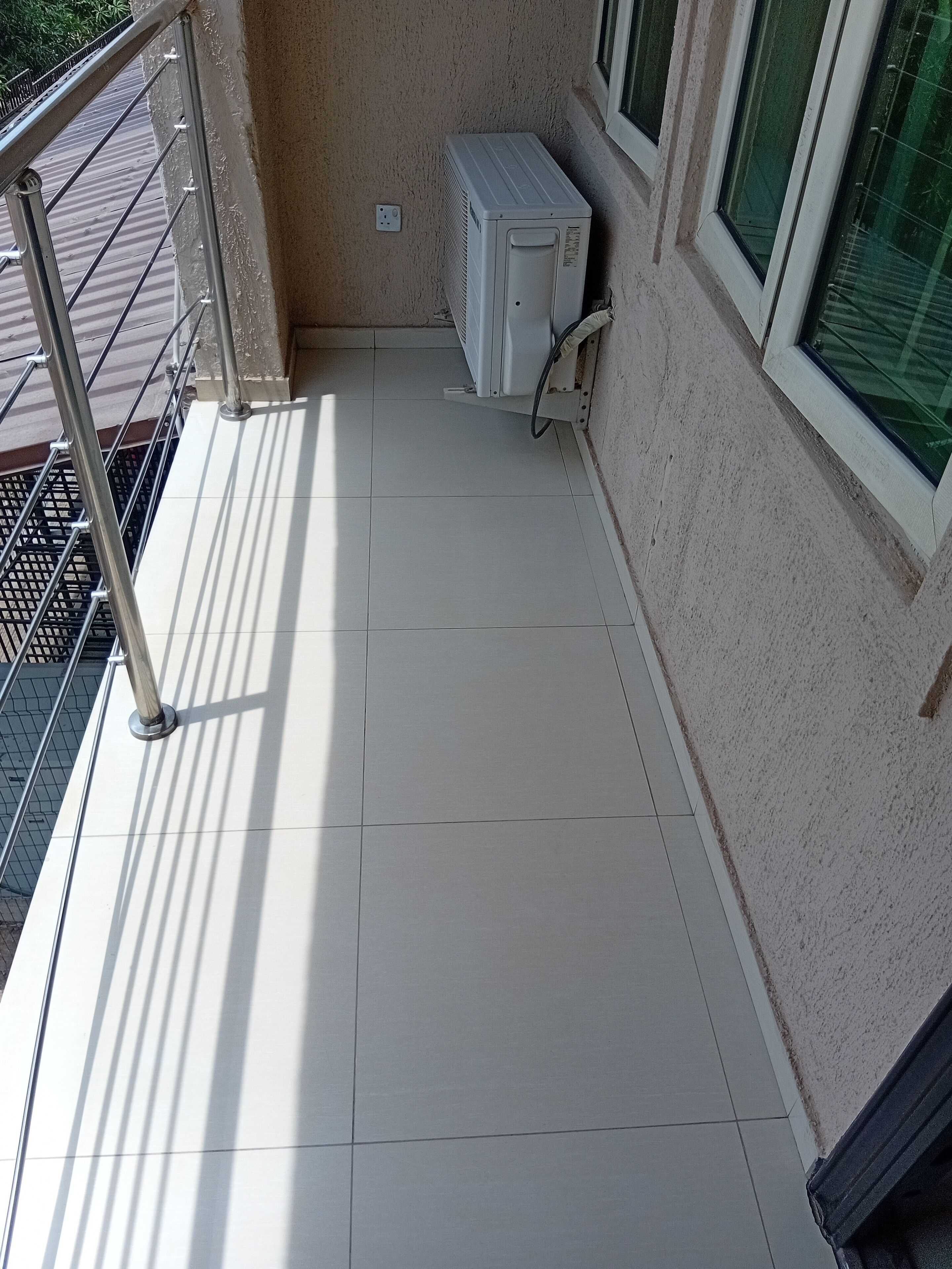 A balcony with a metal railing, a tiled floor, and an air conditioning unit against the wall.