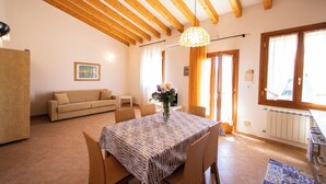 Un salon chaleureux avec un plafond en bois, une table à manger avec des chaises, un canapé et un vase rempli de fleurs.