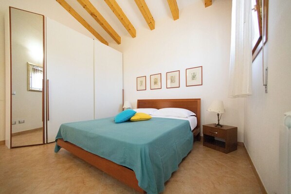 Een slaapkamer met een bed, nachtkastje, spiegel en garderobe.