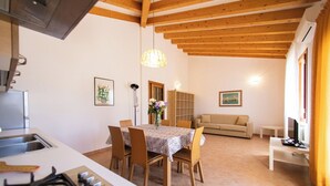 Une cuisine compacte équipée d’une cuisinière à gaz, de poutres en bois au plafond, d’une table à manger avec des chaises, d’un canapé et d’un téléviseur.
