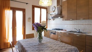 Une cuisine avec des meubles de rangement en bois, une cuisinière et un évier. On y trouve une table à manger recouverte d’une nappe à motifs et agrémentée d’un vase de fleurs.