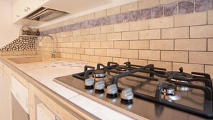 Une cuisine équipée d’une cuisinière à gaz, d’un évier et d’un crédence carrelée.