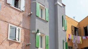 Un immeuble doté de nombreuses fenêtres, dont certaines sont pourvues de volets, et d’un petit balcon. On y voit une corde à linge sur laquelle est étendu du linge, et un vélo est garé à l’extérieur.