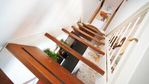 Una escalera con barandas de madera y vistas a una habitación con pared de piedra y una planta.