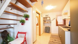 Una cocina con vigas de madera, una silla roja, plantas en macetas y piso de baldosas.