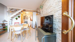 Una sala de estar moderna con una pared de piedra, un televisor, un área de comedor con una mesa y sillas, y una escalera que conduce a otro nivel.