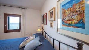 Un dormitorio con cama, ventana con vista al mar y varias fotografías enmarcadas en la pared.