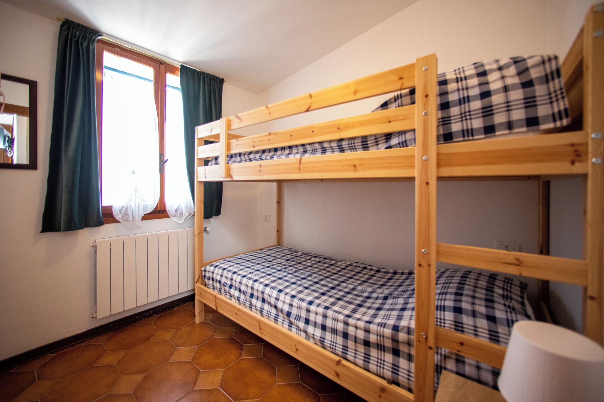 Une chambre avec un lit superposé, une fenêtre, des rideaux et un radiateur.