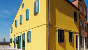 A yellow building with multiple windows and doors, a stone-paved ground, and a clear sky. - Dimora Stella  -apeliving- Pellestrina Ve (Venice)