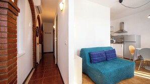 A narrow hallway with a brick wall on one side and a teal sofa with plaid pillows in the living area.