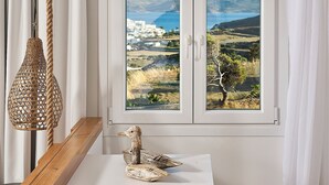 Una stanza con vista sul paesaggio costiero, una lampada in rattan sospesa e un tavolo di legno con una scultura a forma di anatra.