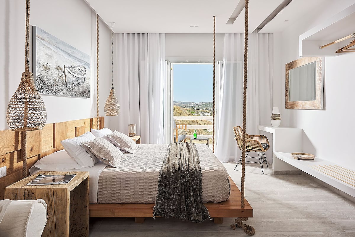 Une chambre à coucher moderne, avec un lit, des tables de chevet, une chaise et une vue sur l’extérieur.