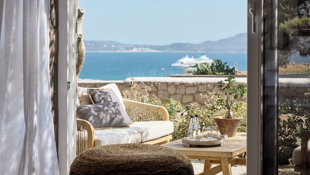 Angolo esterno accogliente con vista sul mare, un muro in pietra e un tavolo di legno con un vassoio.