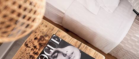 Una revista sobre una mesa de madera, una cama blanca y una cesta tejida.