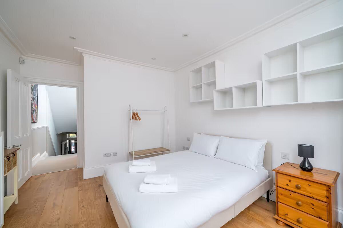 Een slaapkamer met een groot bed, witte muren, houten vloeren en ingebouwde planken.