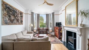 A spacious living room with a large sofa, a fireplace, a ceiling fan, and a large painting on the wall. - Stunning house near Notting Hill (London)