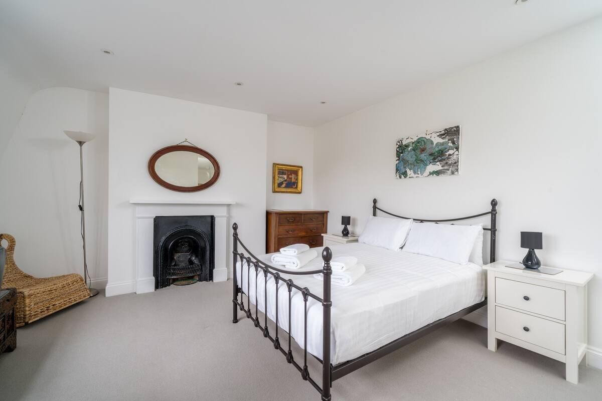 A bedroom with a four-poster bed, a nightstand, a dresser, a fireplace, and a painting on the wall.