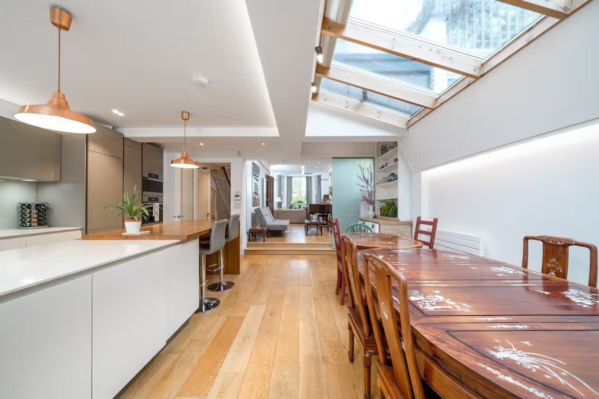 A modern kitchen with a wooden dining table and chairs, a large window, and a view of the city.