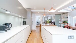 A modern kitchen with white cabinetry, a central island, pendant lighting, and a view into the dining area. - Stunning house near Notting Hill (London)