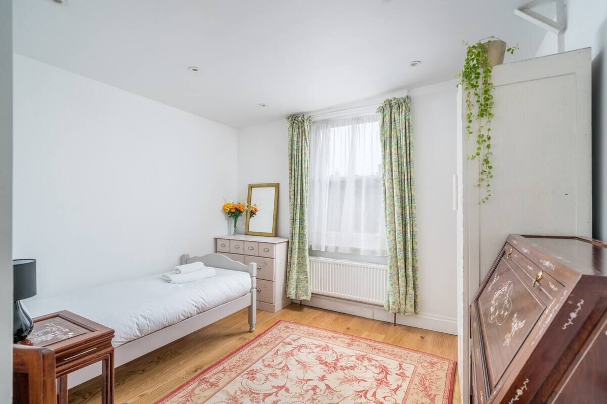 Ein Schlafzimmer mit einem Einzelbett, einem Schminktisch, einem Heizkörper und einem Fenster mit Vorhängen.