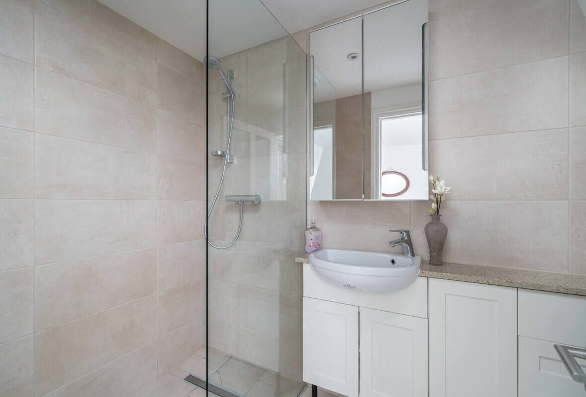 A modern bathroom with a glass shower enclosure, a white sink, and a mirror above it.
