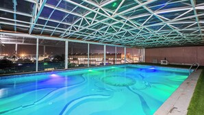 Una piscina interna con tetto in vetro e vista sulla città di notte.