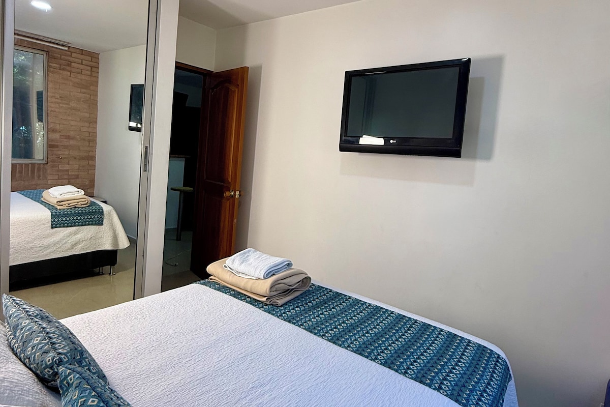 Habitació d'hotel amb llit, televisió penjada a la paret i mirall.