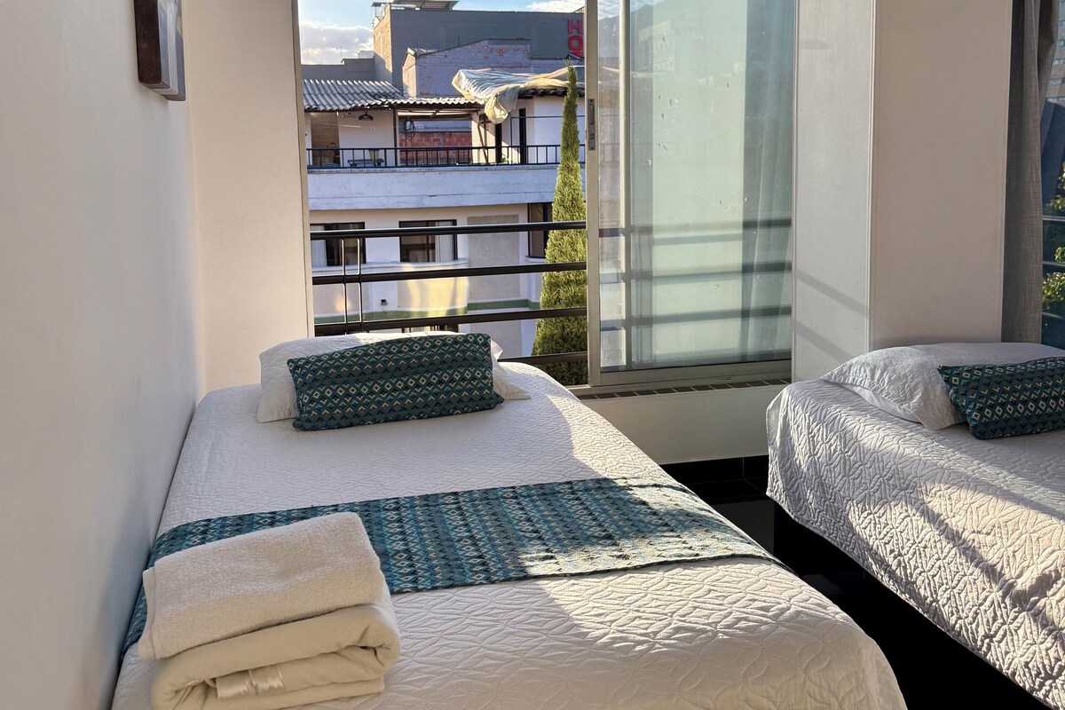 Une chambre d’hôtel avec deux lits, une grande fenêtre et une vue sur les bâtiments environnants.