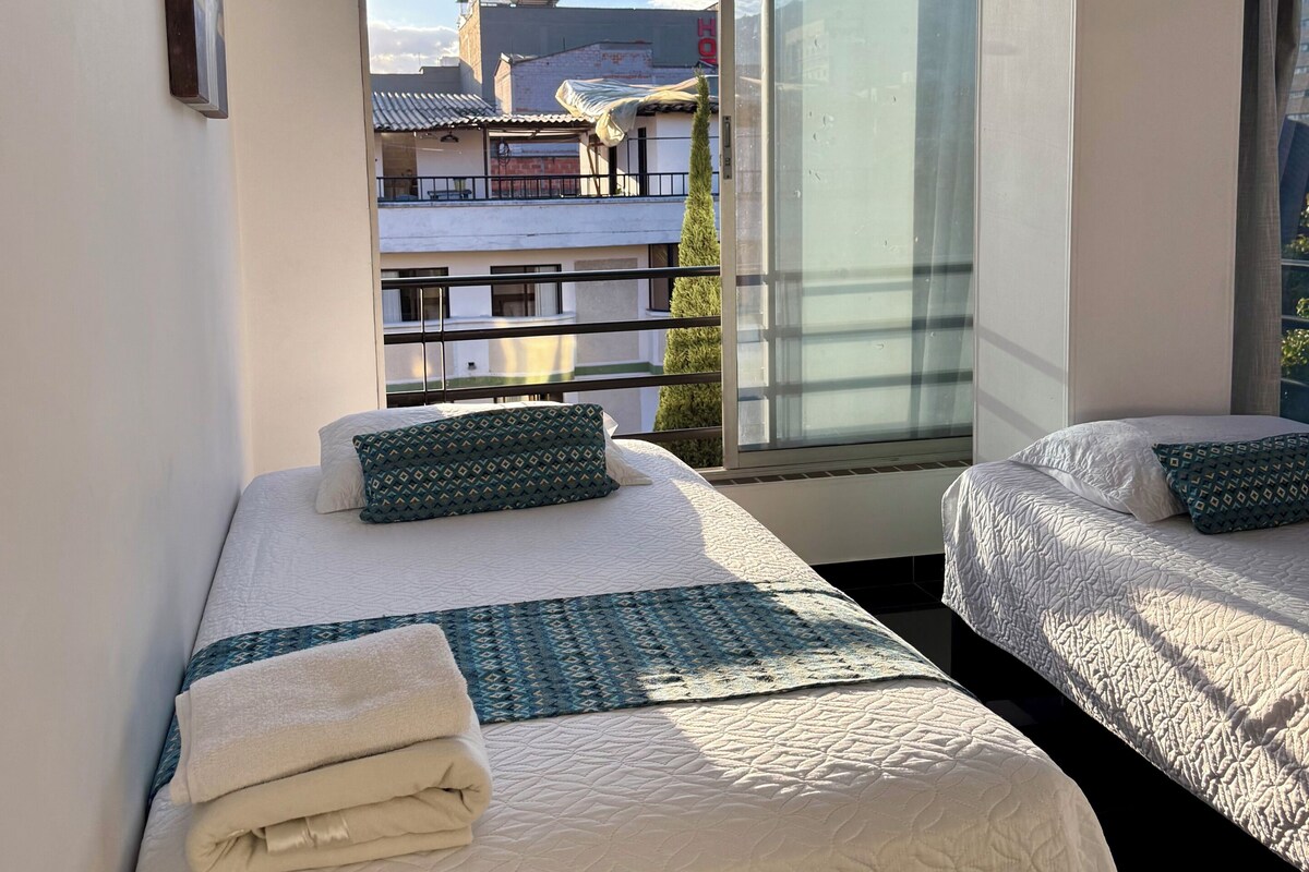 Ein Hotelzimmer mit zwei Betten, einem großen Fenster und Blick auf Gebäude.