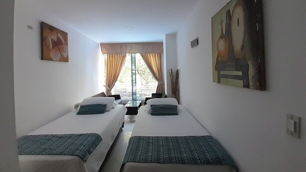 A hotel room with two beds, a large window with curtains, and artwork on the walls. - Apartahotel Montes  (Medellin)