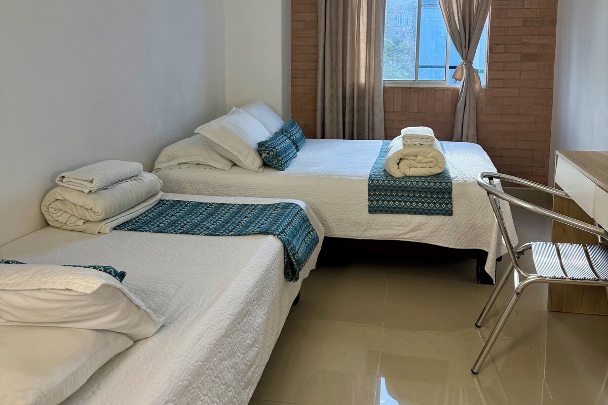 A hotel room with two beds, a chair, and a window with curtains.