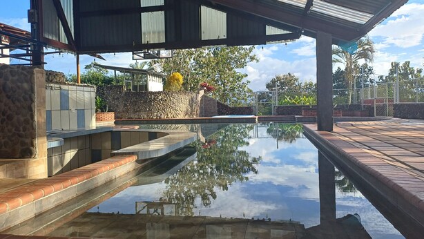 Ein Schwimmbecken mit spiegelklarer Oberfläche, umgeben von Steinmauern und einem überdachten Bereich mit Metallverkleidung.