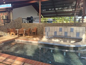 En udendørs terrasse med stenvæg, pool og integreret køkkenområde.