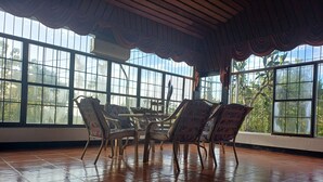 Ein geräumiges Zimmer mit großen Fenstern, Fliesenboden und einem Tisch mit Stühlen.