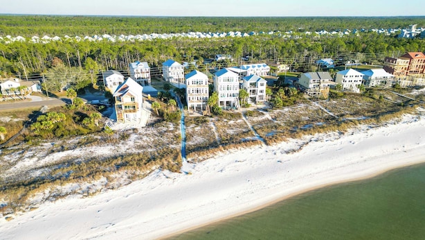 An aerial view of a coastal residential area with beachfront properties, including multi-story houses with blue roofs and a sandy beach in the foreground. - Watermark Way -Private pool- Elevator Private Beach access (Port St. Joe)