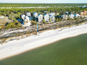 Vista aérea de una zona residencial costera con propiedades frente a la playa, incluyendo casas de varios pisos con techos azules y una playa de arena en primer plano.