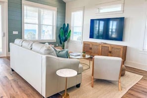 Una sala de estar con un sofá, un sillón, una mesa de centro y un televisor en la pared.