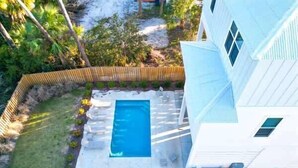 A residential property with a swimming pool, a fenced yard, and a white house.