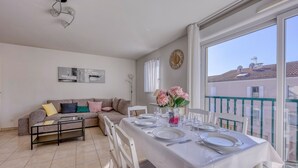 A dining area with a table set for four, a sofa, and a balcony with a view. - L'Orée du Cap - Climatisé proche plage (Six-Fours-les-Plages)