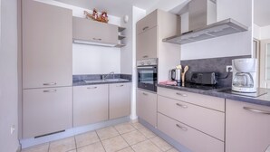 A modern kitchen with beige cabinets, a stainless steel range hood, a built-in oven, a toaster, and a coffee maker. - L'Orée du Cap - Climatisé proche plage (Six-Fours-les-Plages)