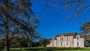 Un edificio in pietra di due piani con una facciata simmetrica, numerose finestre e un prato ben curato davanti.